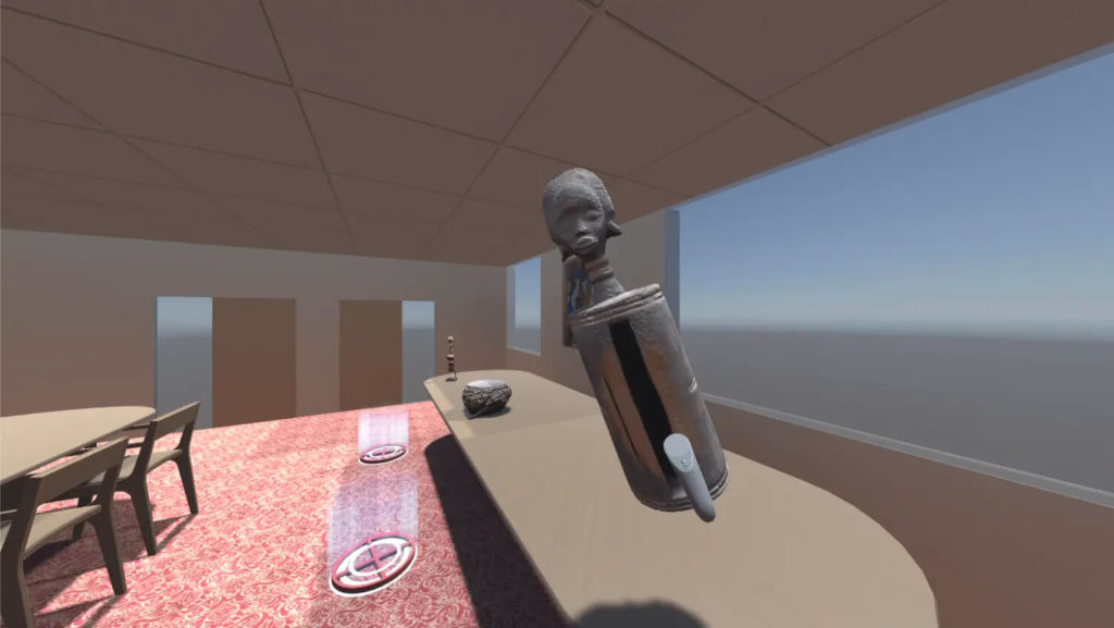 A virtual recreation of the Blockson reading room with red-patterned carpet, tile ceiling, 2 tables, and glassless windows that look out onto the blue empty Unity Game Engine space. There are 3D models of African Instruments on one of the long tables. A slot drum is floating in air, being lifted by a 3D representation of the VR controller.