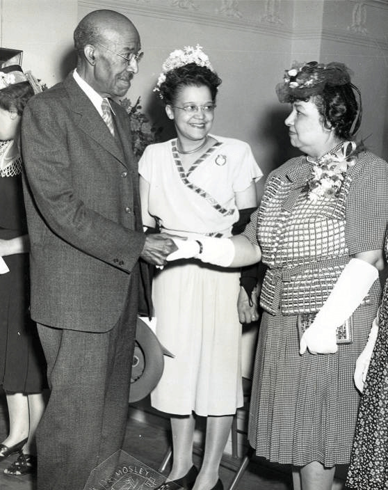 A black and White photo of three African American people in clothing from the 1940’s. Laura Wheeler Waring is the figure on the right and is shaking hands with Dr. Nathan F. Mossell while Sadie T.M. Alexander stands in the center and smiles at Wheeler-Waring.